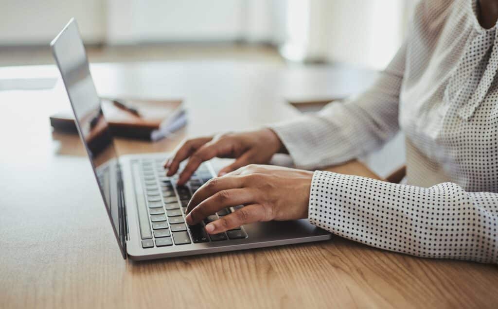 An unrecognized businesswoman sitting at her desk, typing on her laptop computer with a pen and note book close by. Stock photo